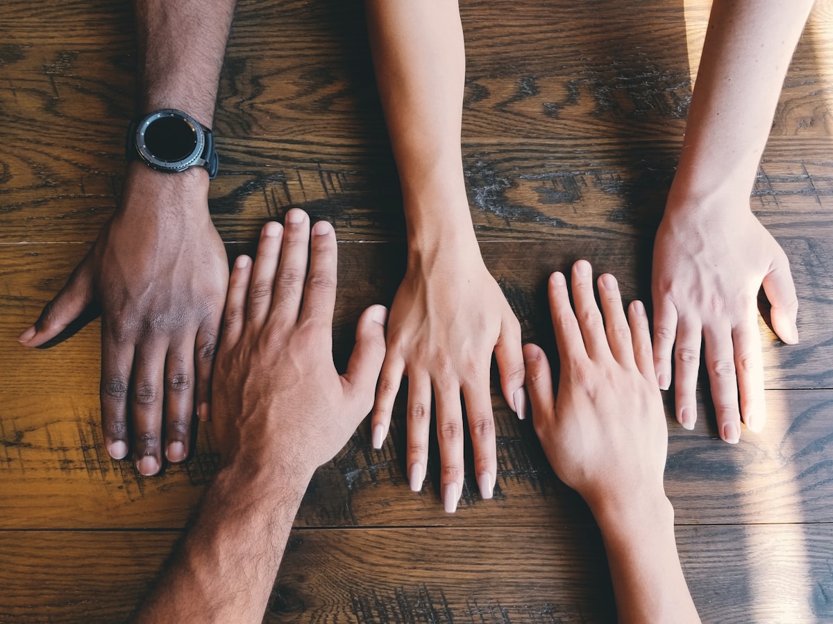 Hände verschiedener Menschen zusammengelegt als Symbol für Teamwork und Engagement