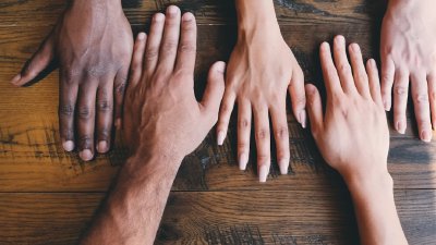 Hände verschiedener Menschen zusammengelegt als Symbol für Teamwork und Engagement